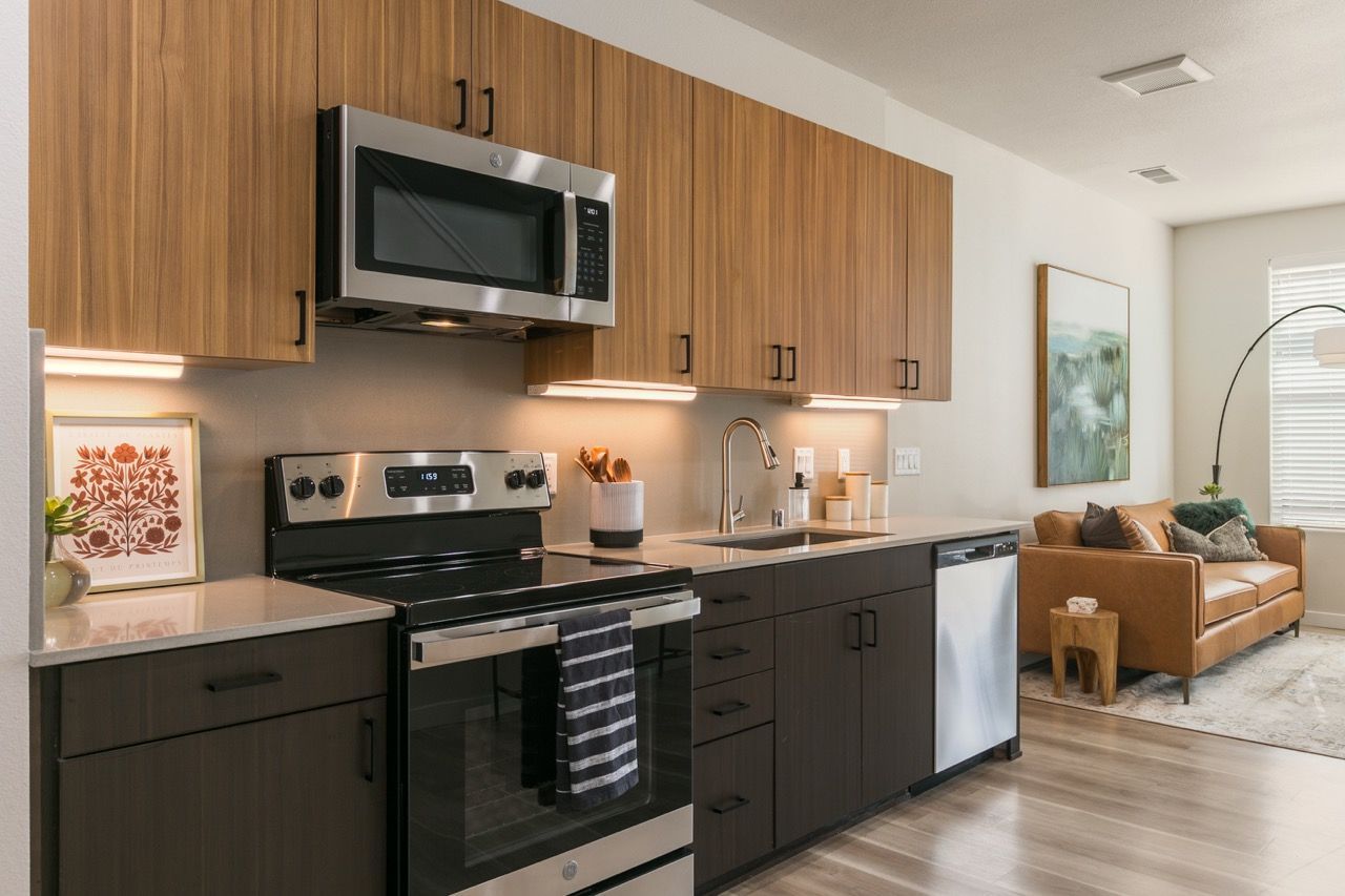 Modern apartment kitchen with stainless steel appliances and wooden upper cabinets.