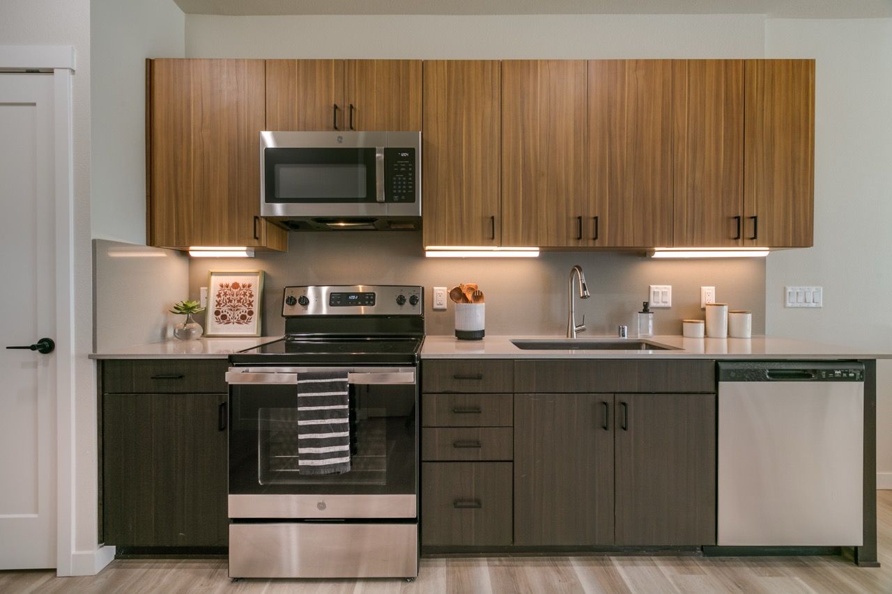 Modern apartment kitchen with wood upper cabinets, stainless steel appliances, and a double sink.