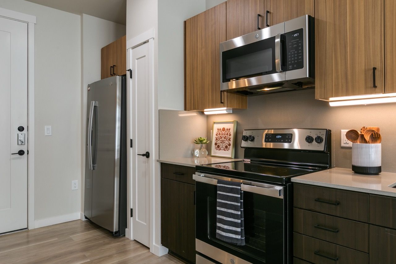 Modern kitchen with stainless steel refrigerator, microwave, oven, and wood-toned cabinets.