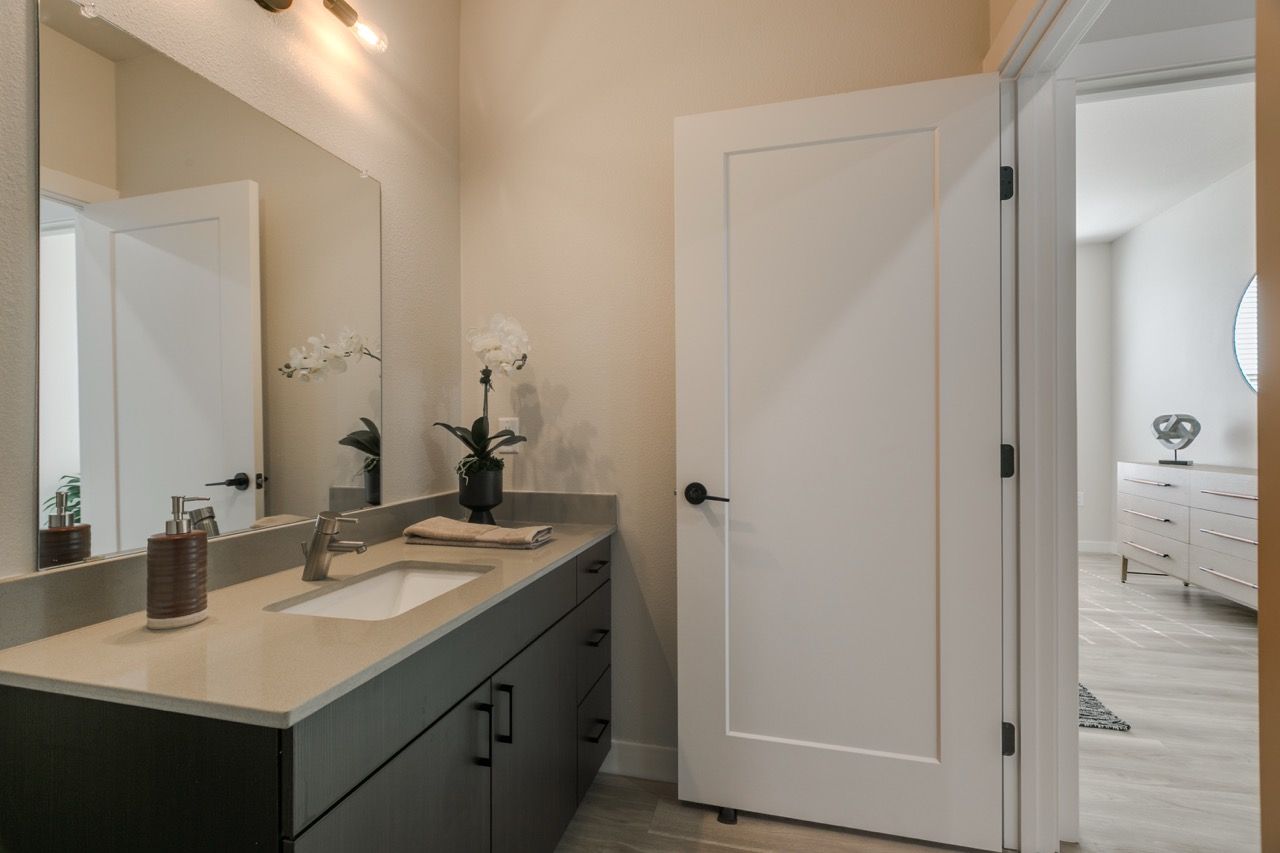 Bathroom vanity with sink, faucet, and mirror; door opens to a bedroom.