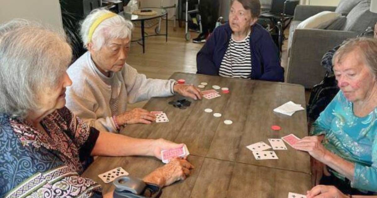 Four elderly women playing cards at a table indoors. Coral Tree Care Home assisted living near Redondo Beach, CA.