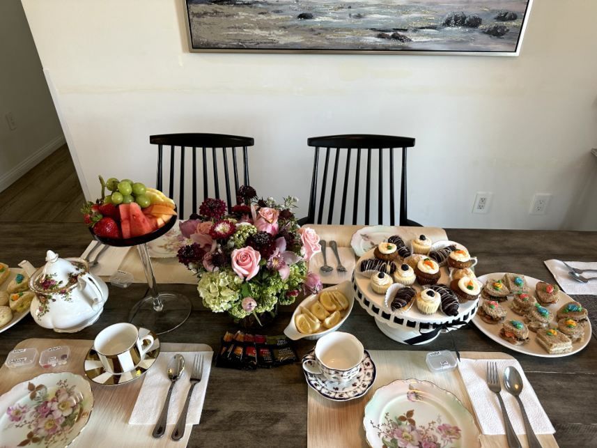 Tea party table set with pastries, fruit, and flowers. Two striped chairs in the background. Respite care in Lomita, CA.