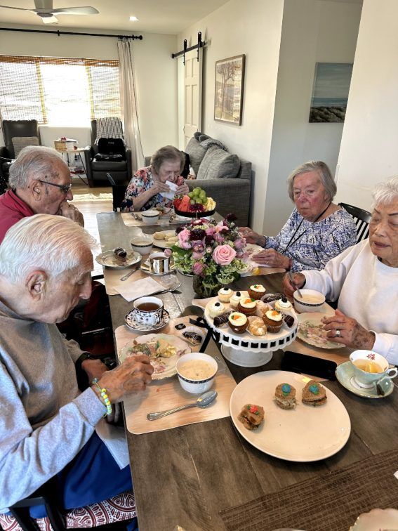 Elderly people at a table, enjoying tea and desserts. Interior shot, bright. Pepper Tree Assisted Living in Lomita, CA.