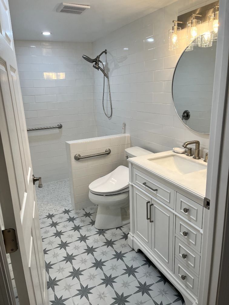 Modern white bathroom with star patterned floor tiles, shower, toilet, and vanity with a round mirror.