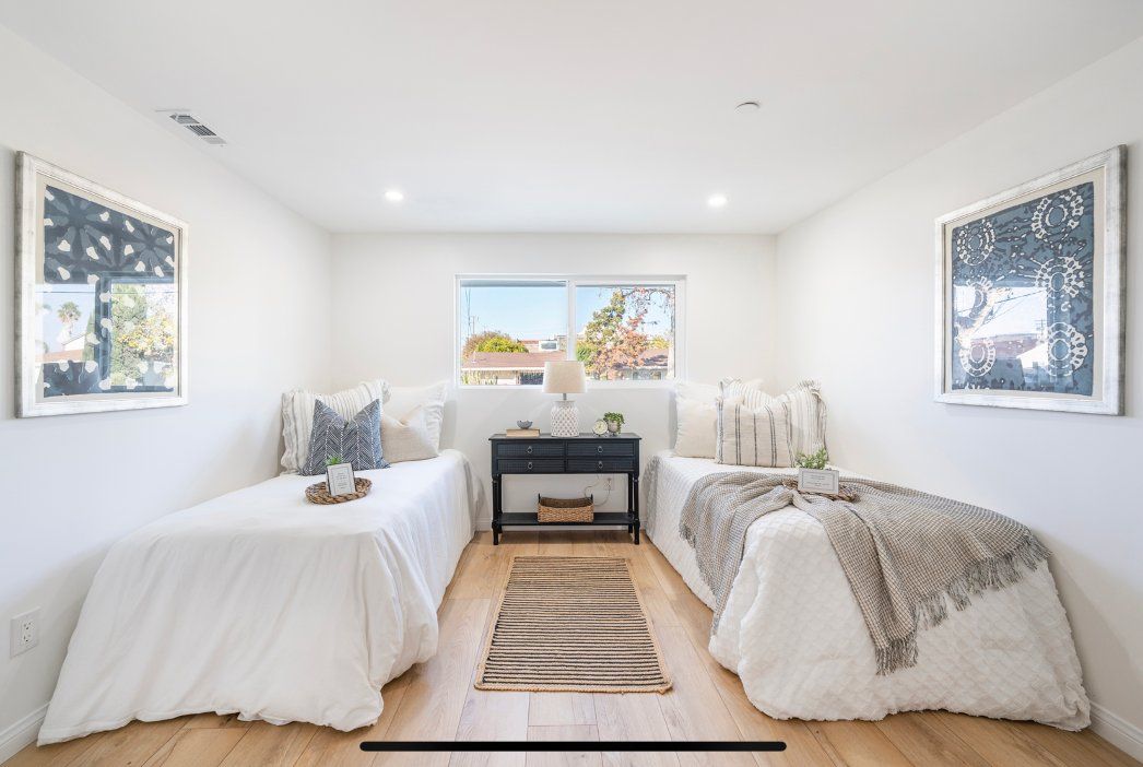 Two twin beds in a white-walled room with artwork, a nightstand, and a window. Pepper Tree Assisted Living in Lomita, CA.