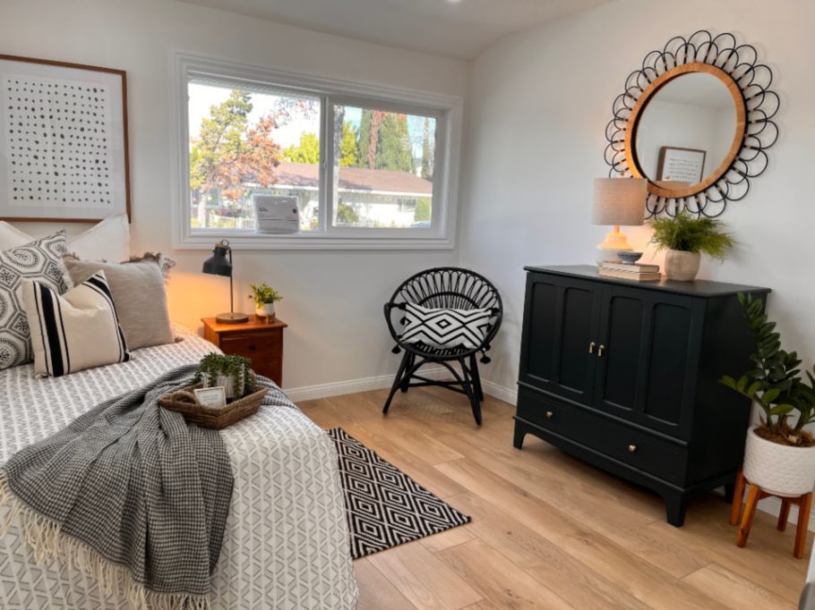 Bedroom with bed, black cabinet, chair, and window, decorated in neutral tones.