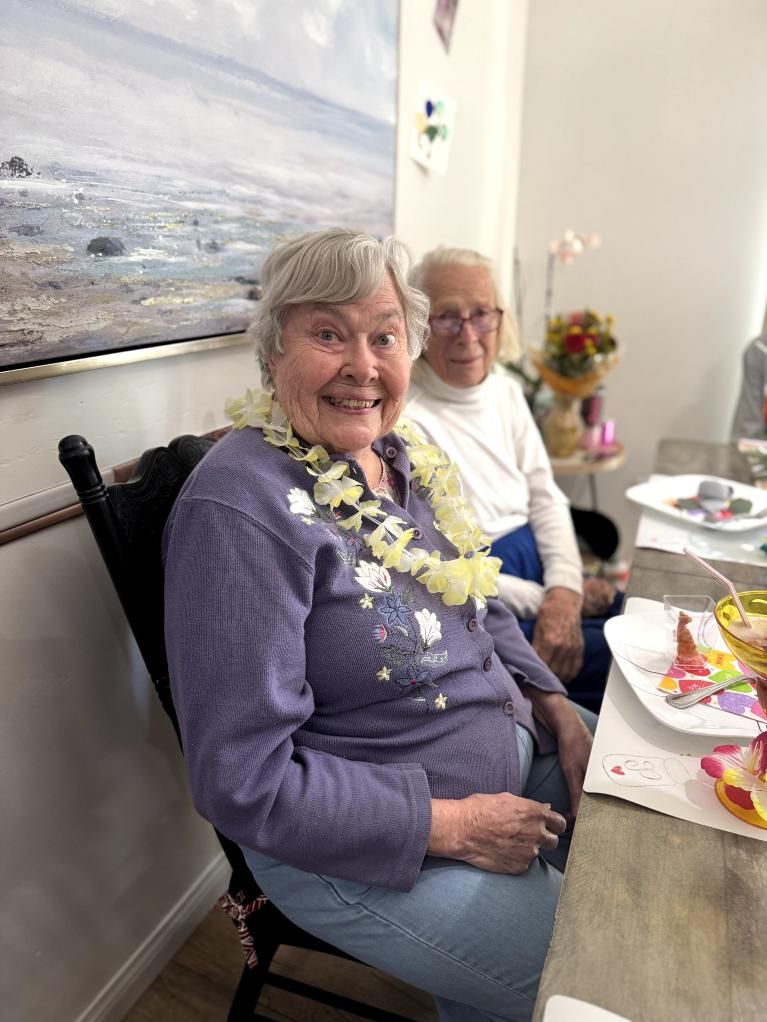 A woman with a white flower lei smiles next to an older man. Pepper Tree Assisted Living in Lomita