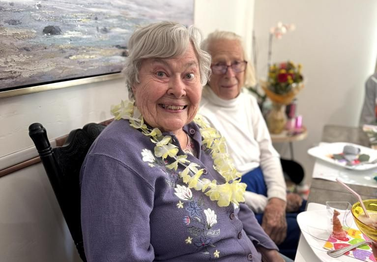 Two smiling elderly women near a table with food. Understanding senior care in Lomita, CA.