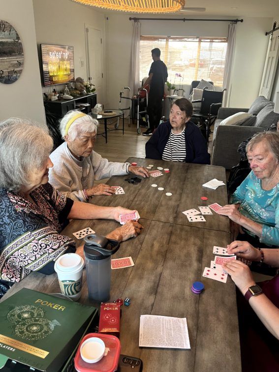 Four older women playing cards around a wooden table. Pepper Tree Assisted Living in Lomita, CA.