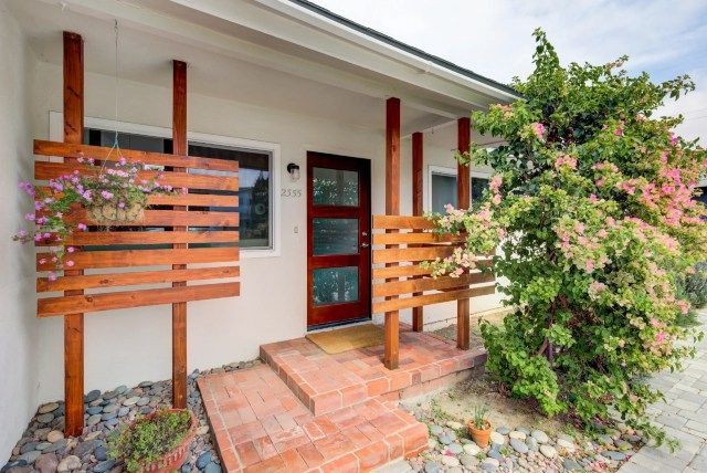 Front of a modern home with red door, wooden details, and lush bougainvillea.