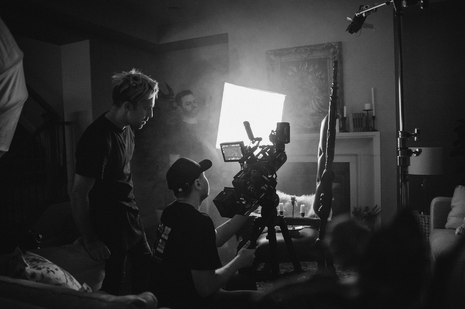 A black and white photo of a man holding a camera in a living room.