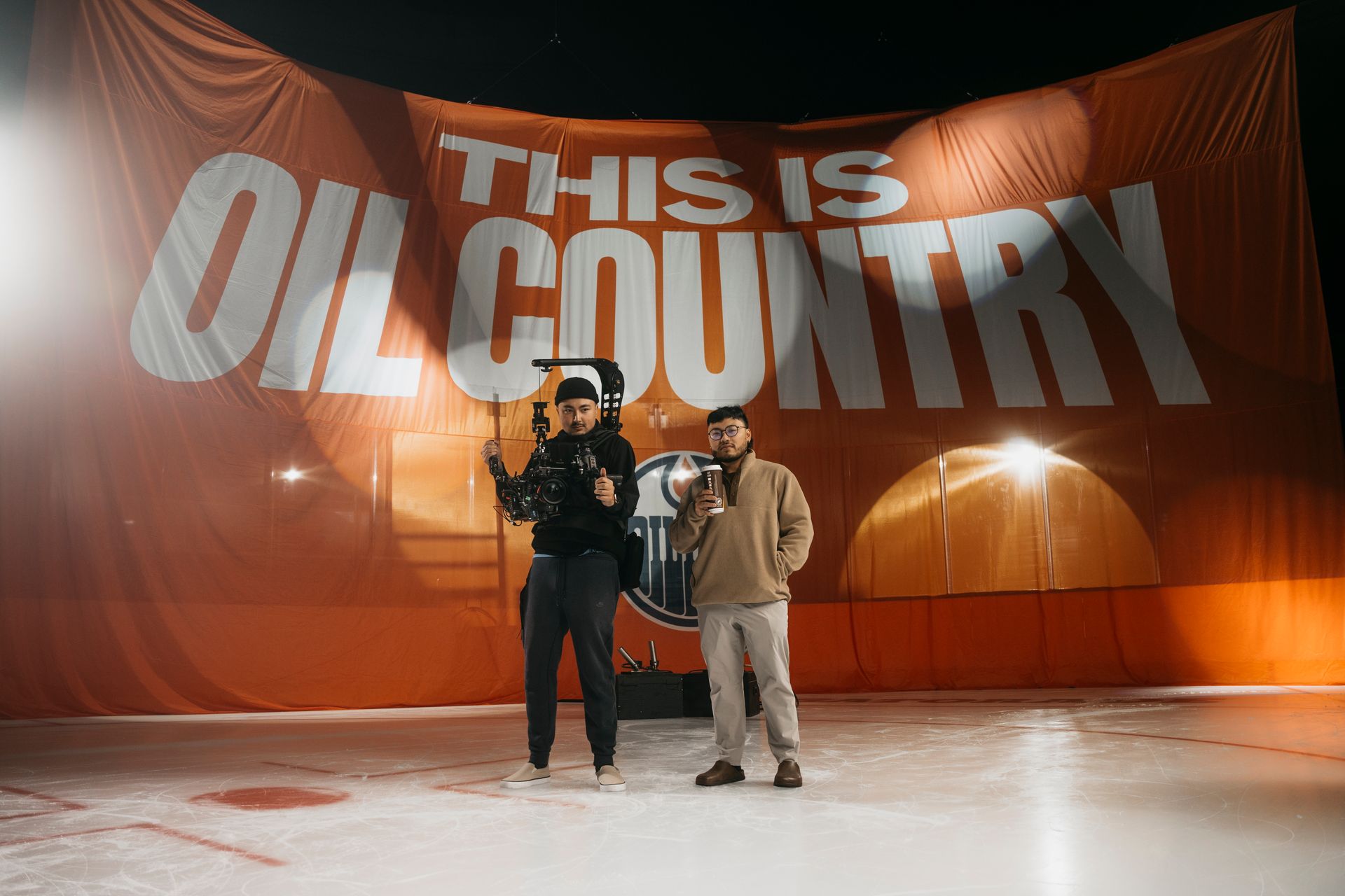 Two men are standing in front of a large orange banner that says `` this is oil country ''.