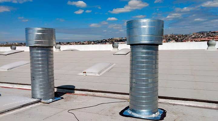 Dos salidas de aire plateadas sobre un tejado plano con un cielo azul claro de fondo.