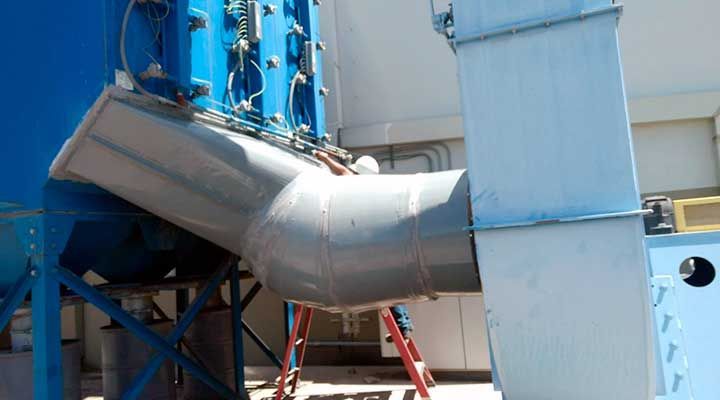 Un sistema de ventilación industrial grande, azul y gris, con un conducto en ángulo; una persona trabaja en el sistema.