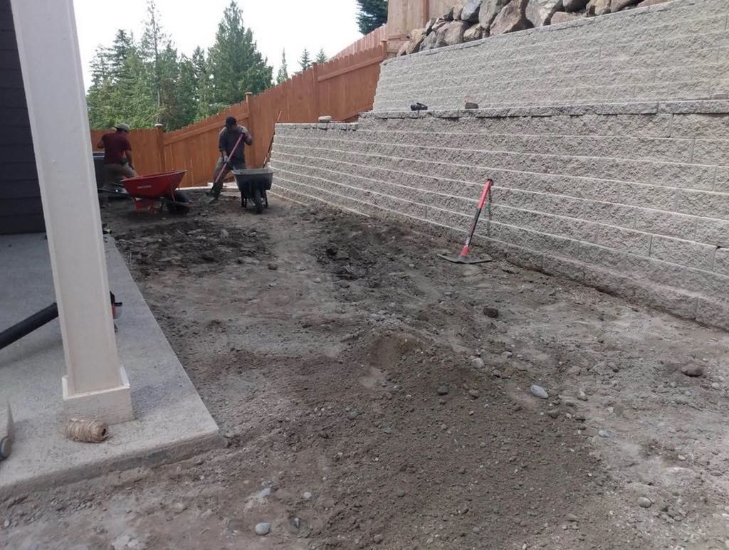 A man is pushing a wheelbarrow in front of a brick wall.