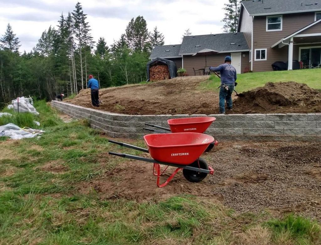Two red wheelbarrows are sitting in the dirt in front of a house.