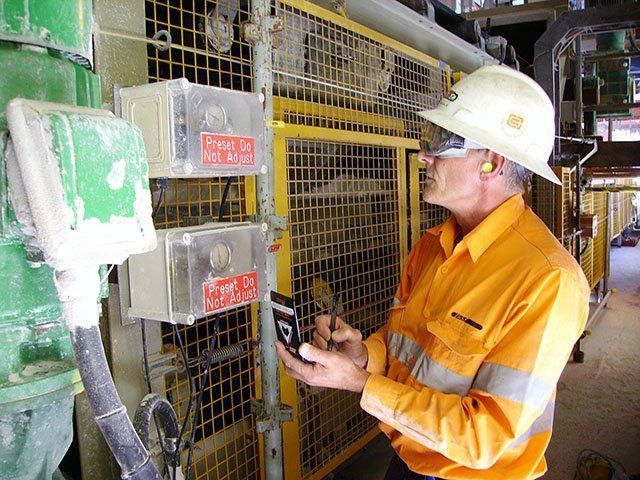 a man wearing a hard hat is looking at a cell phone .