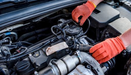 Hands in orange gloves working on a car engine.
