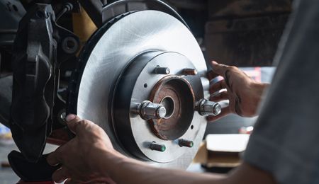 Hands installing a new brake rotor on a car wheel assembly in a repair shop.