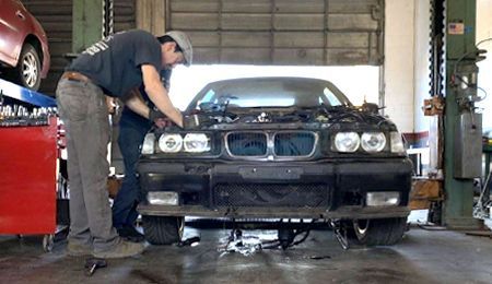 Two mechanics working on a black BMW in a garage, removing parts.
