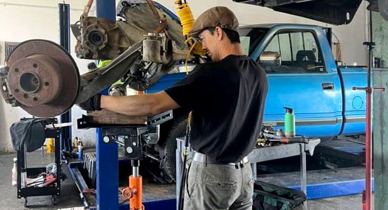 Mechanic working on car lift. Blue truck in background. Workshop interior.