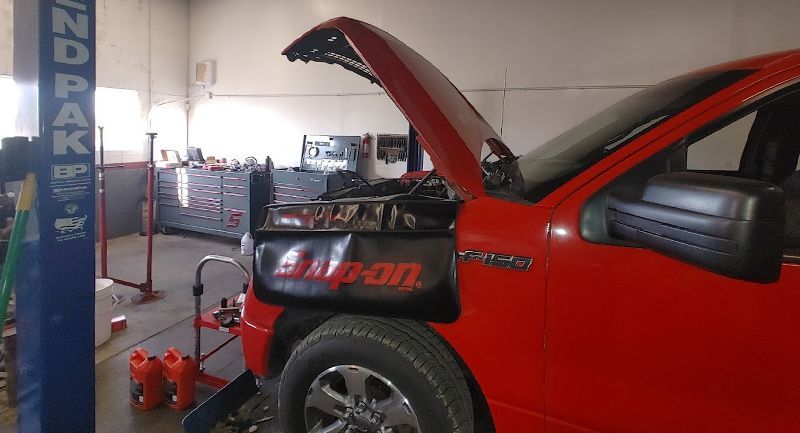 Red pickup truck with the hood open in a repair shop.