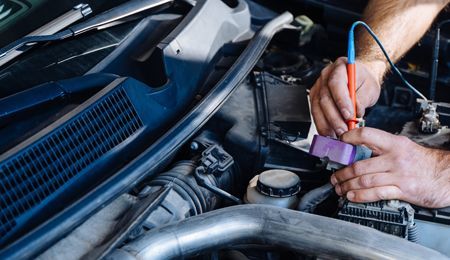Mechanic using a multimeter to test a car's electrical system under the hood.