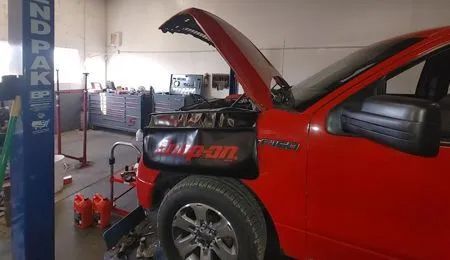 Red Ford truck with hood up in a repair shop.