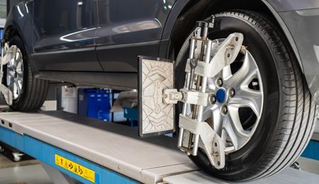Car on a lift with alignment equipment attached to a tire, in a mechanic's shop.