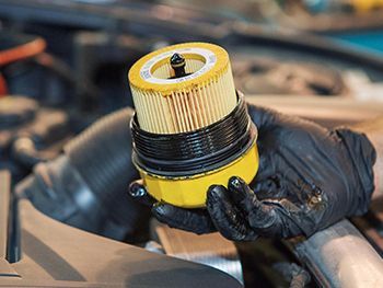 Person wearing gloves holding a used yellow oil filter during car maintenance.