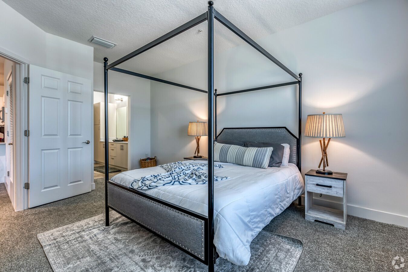 A bedroom with a four poster bed , two lamps , and a rug.