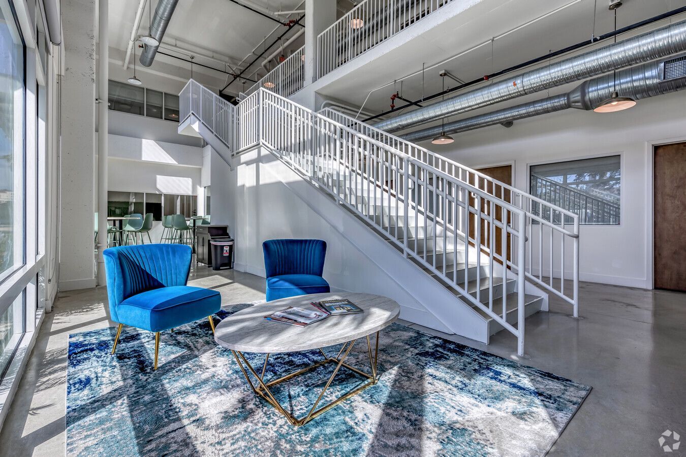 A living room with blue chairs , a coffee table and stairs.