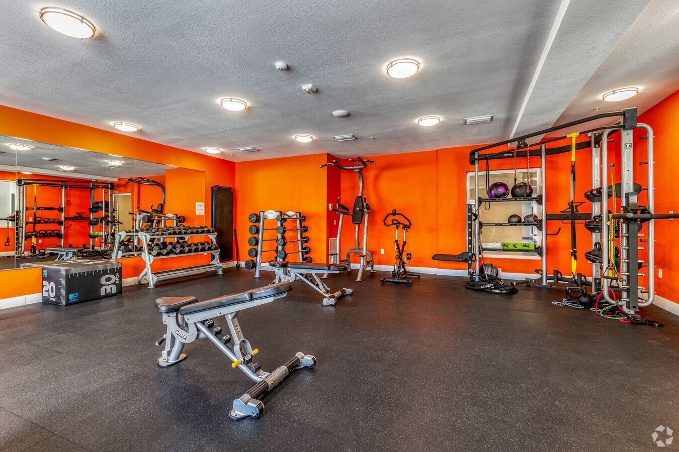 A large gym with orange walls and lots of equipment.