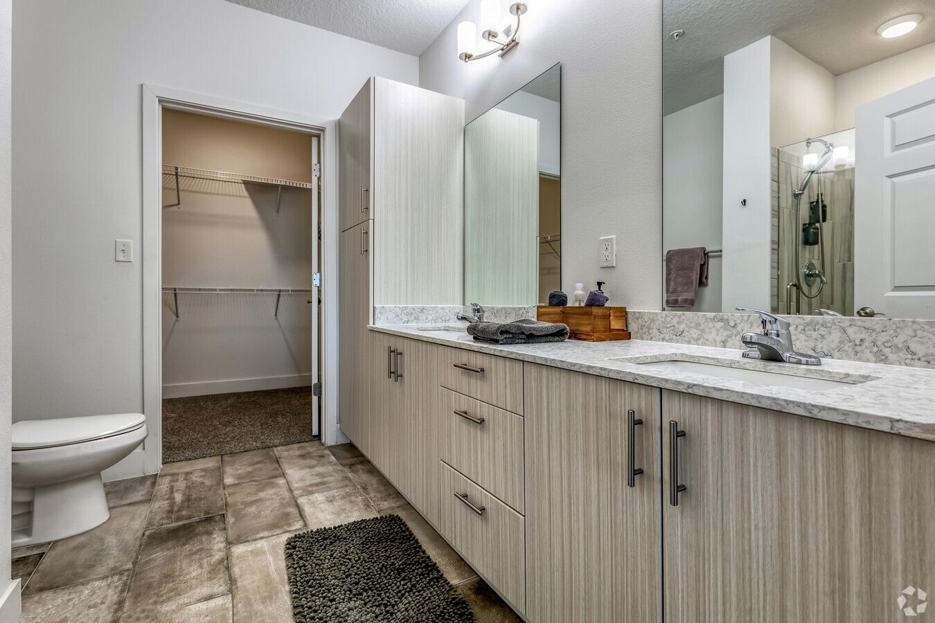 A bathroom with two sinks , a toilet , and a walk in closet.
