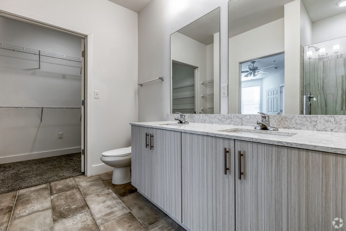 A bathroom with two sinks , a toilet , and a walk in closet.