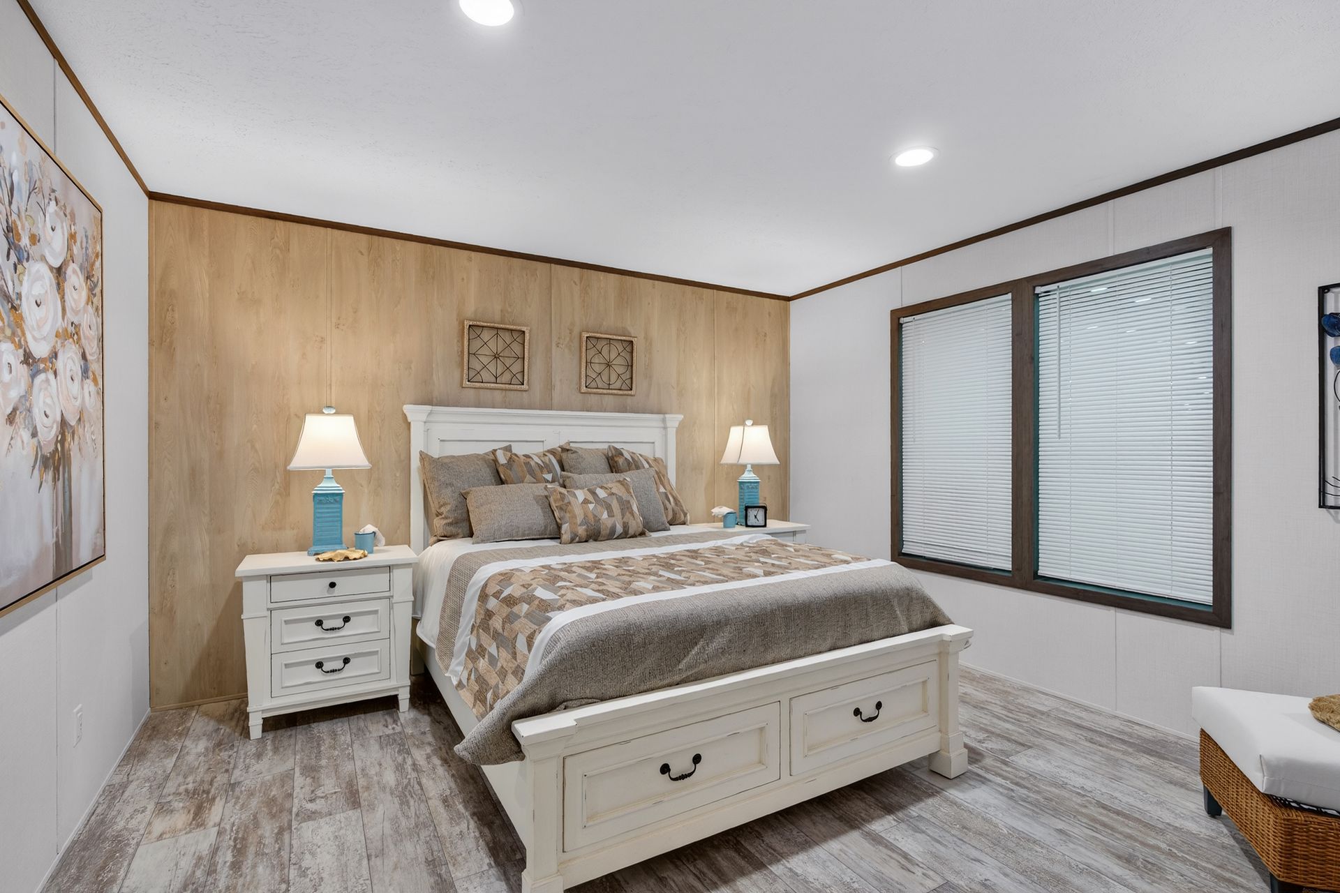 Bright bedroom with a king bed, white nightstands, wood accent wall, and two windows with blinds.