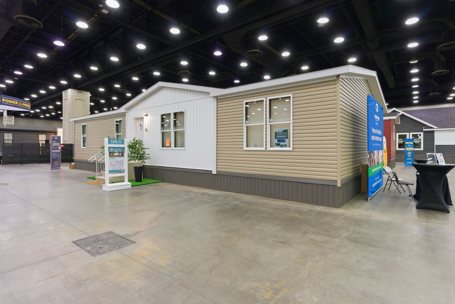 Modern tiny house display booth with white and beige exterior at an indoor expo hall