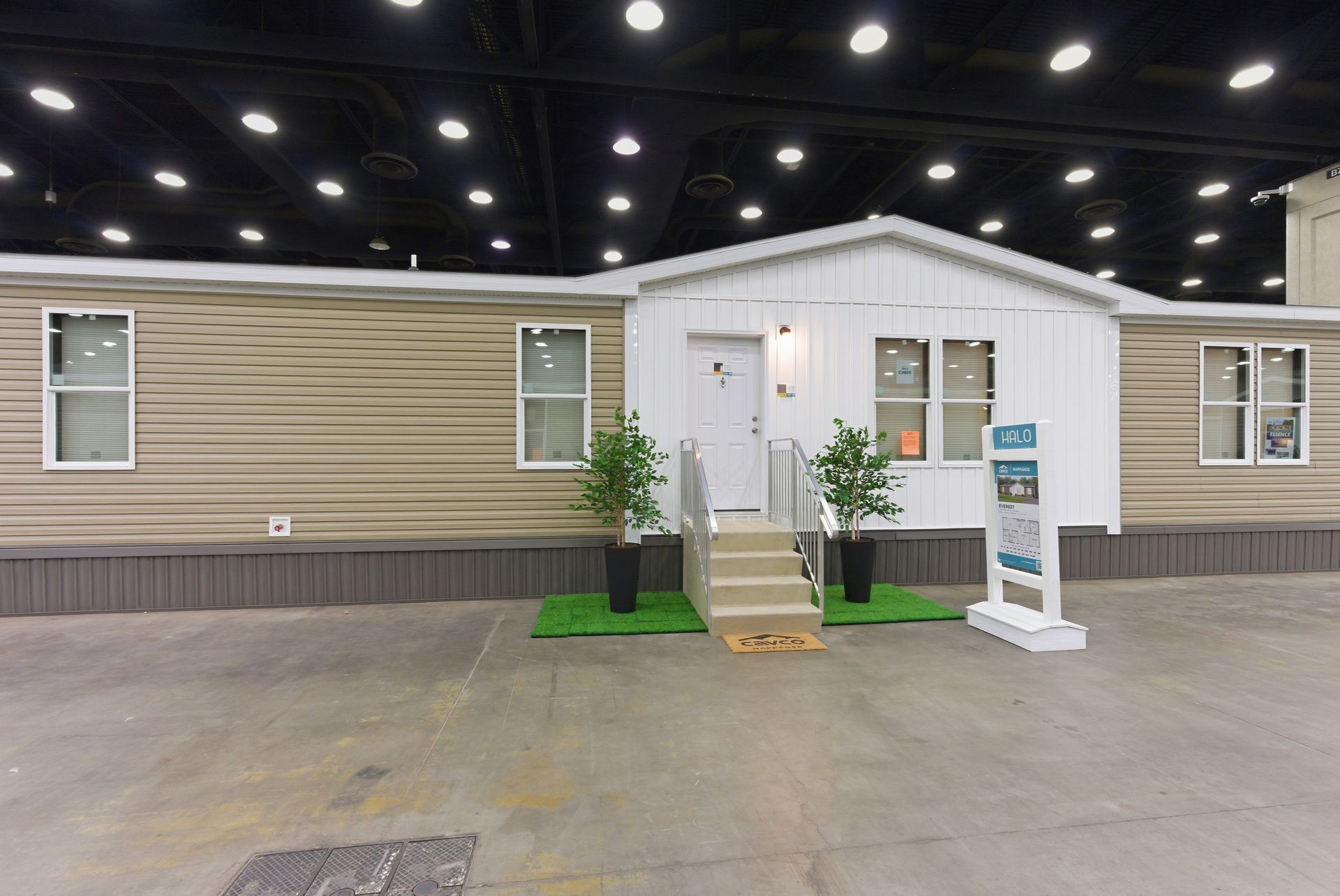 Modular home display with white front door, steps, and small porch inside a showroom