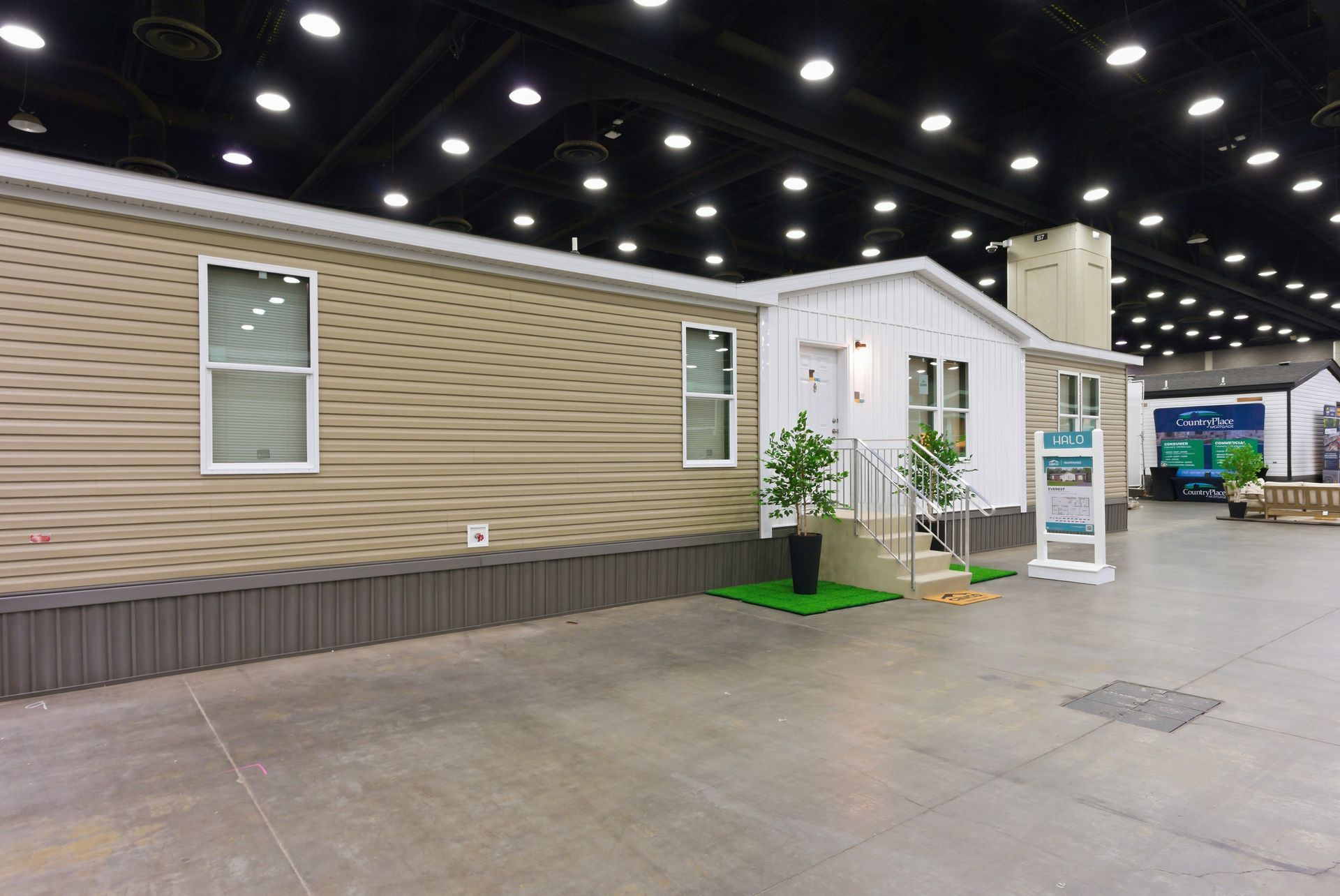 Indoor exhibition hall with tiny house display, beige siding, white trim, and informational signs