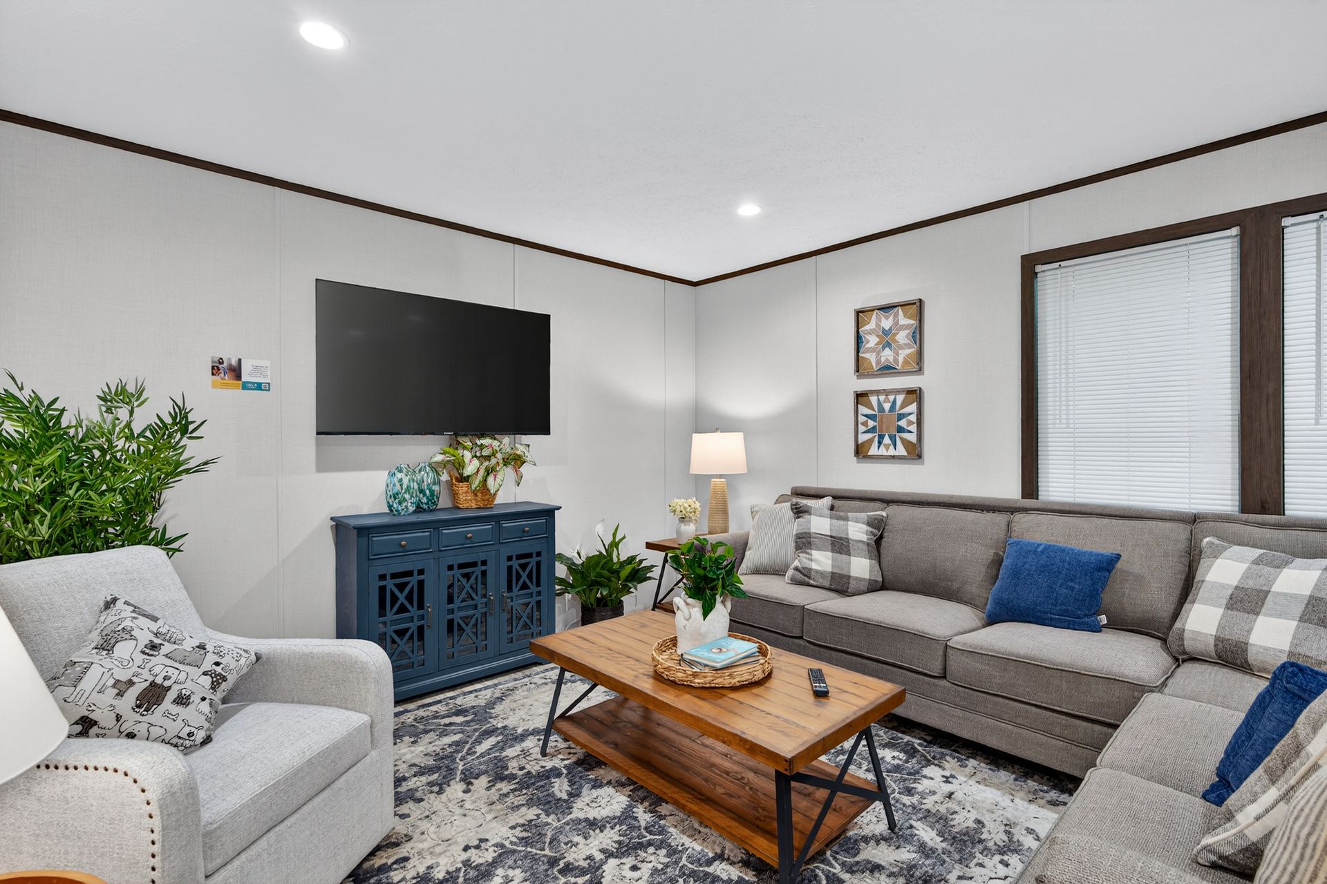 Bright living room with gray sofa, white chair, blue TV console, coffee table, and large windows