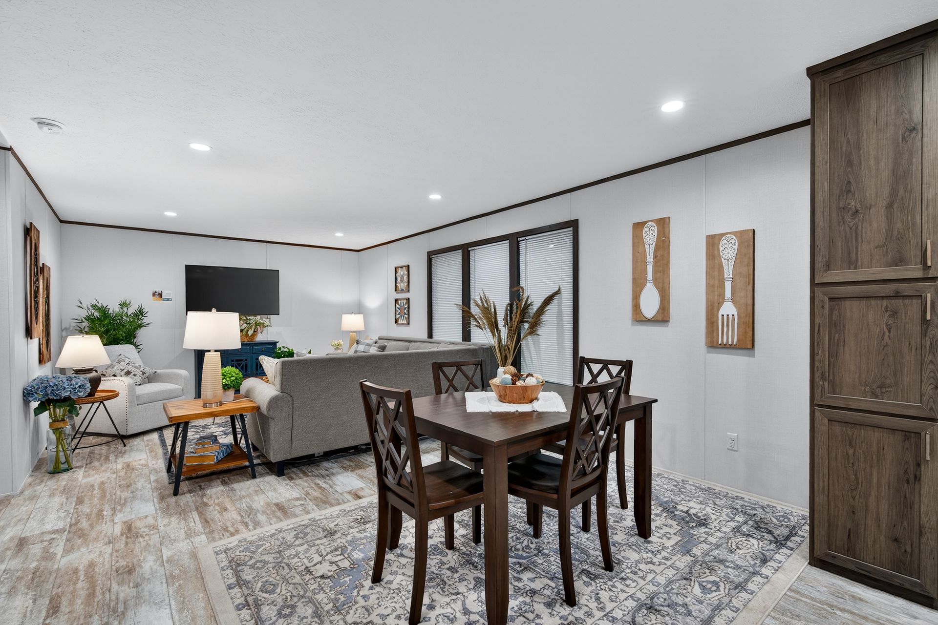 Modern open-concept dining and living room with gray furnishings, wood table, and large patterned rug.