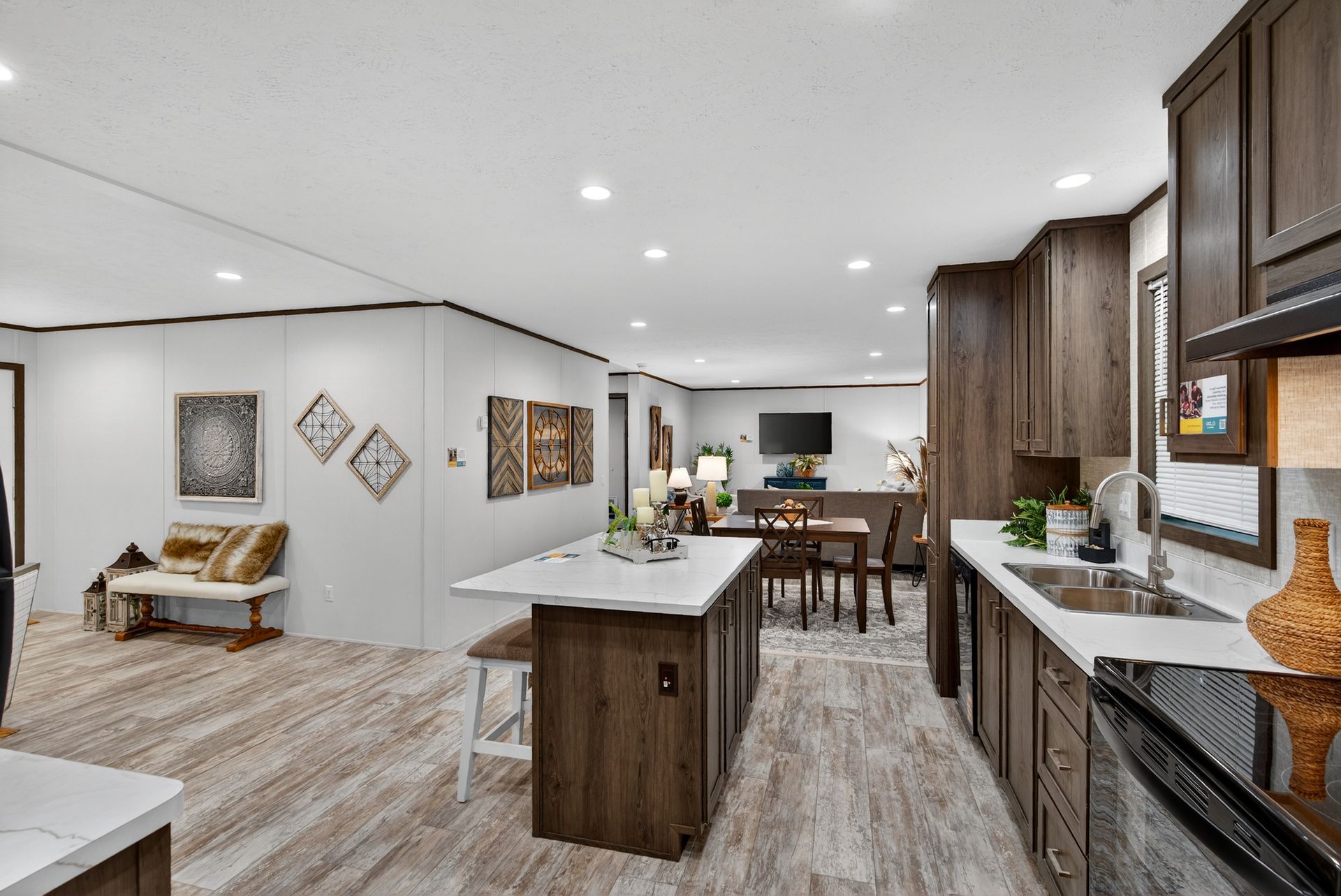 Modern open-concept kitchen and living room with wood cabinets, island, dining table, and sofa under recessed lights