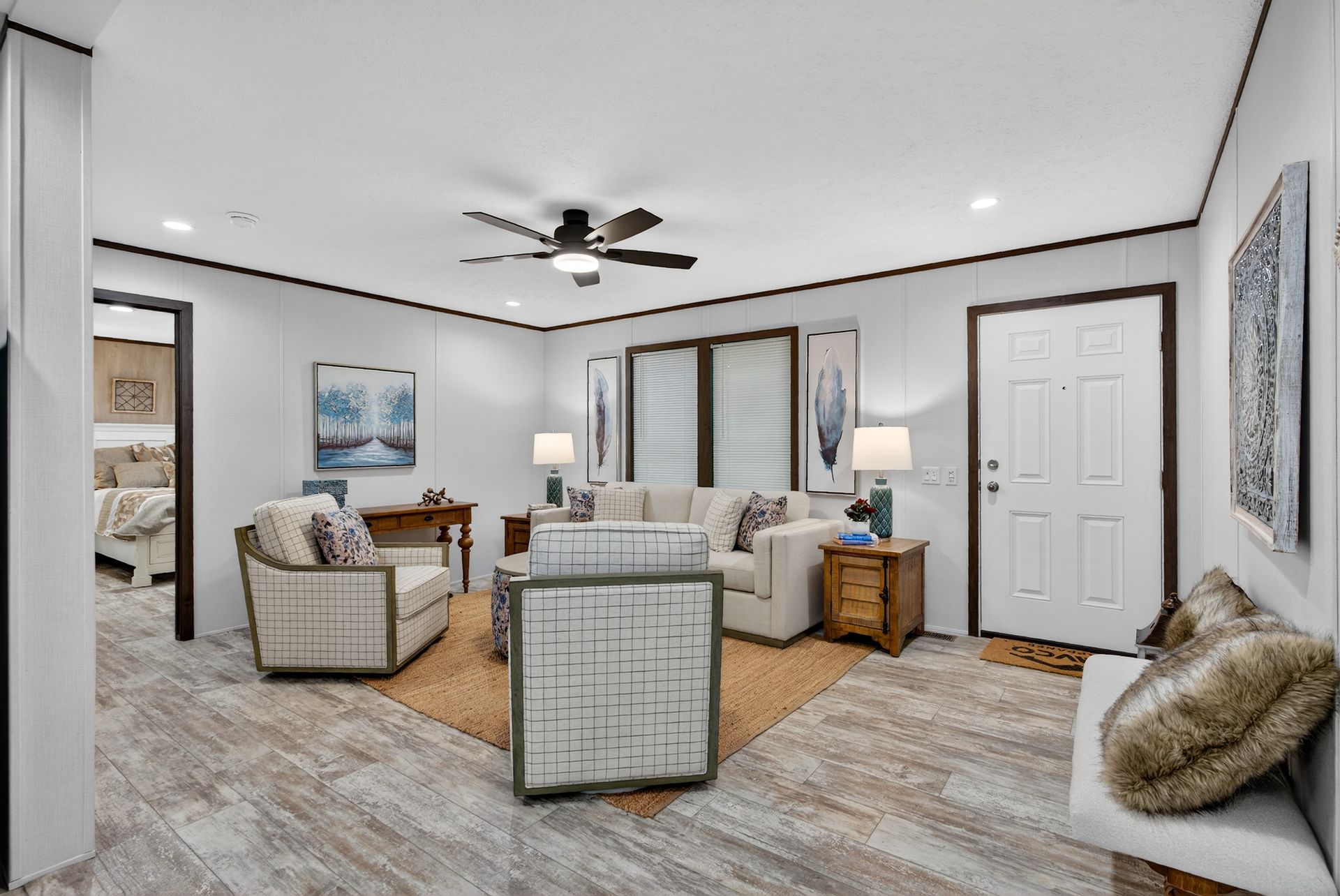 Bright living room with wicker seating, tan rug, ceiling fan, and large windows.
