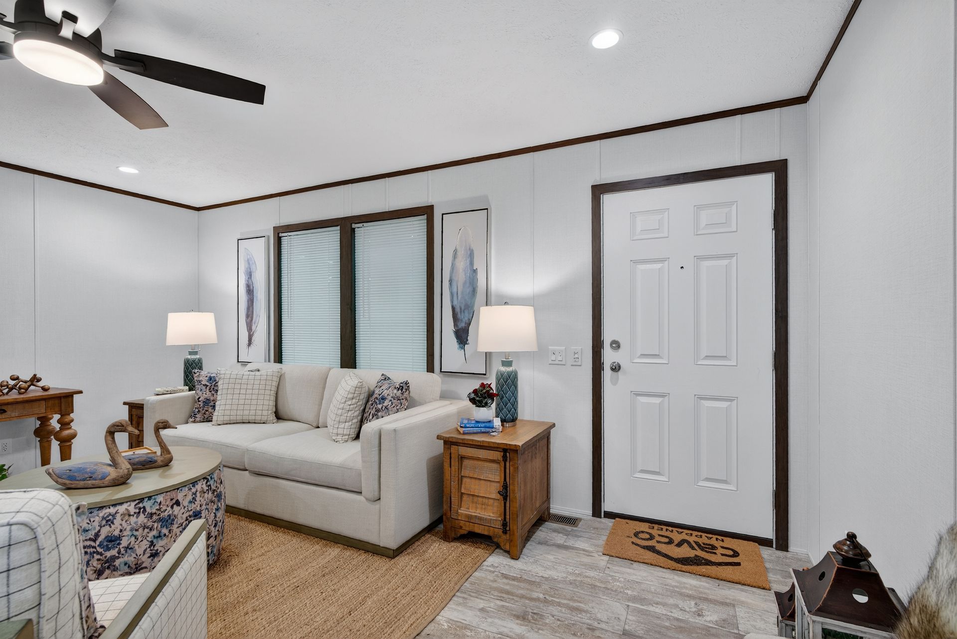 Bright living room with beige sofa, striped curtains, wooden side tables, and front door on a white wall.
