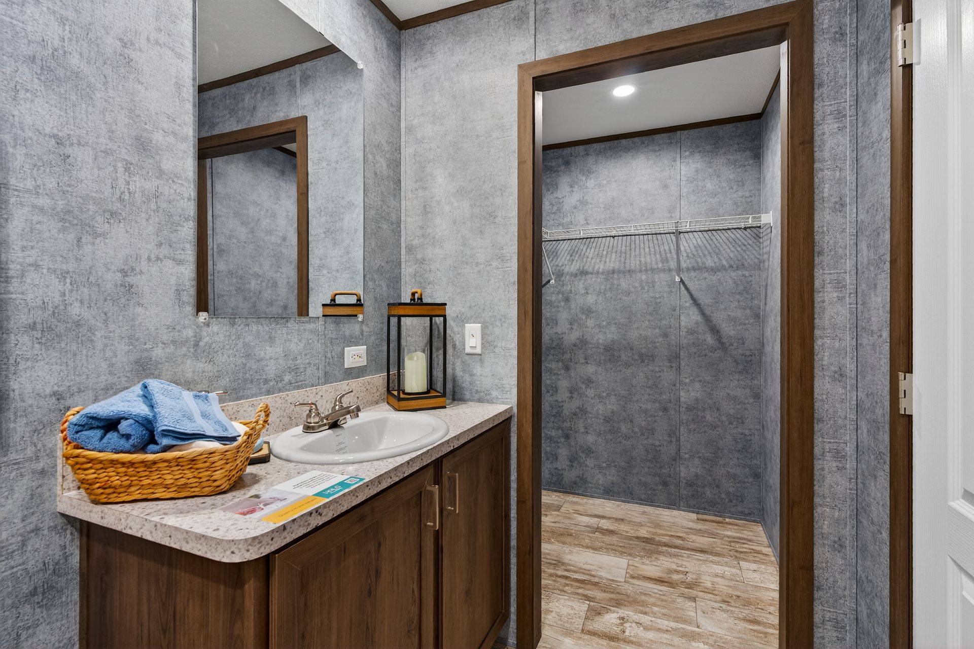 Bathroom vanity with wooden cabinet, marble countertop, basket of towels, and open doorway to tiled shower area