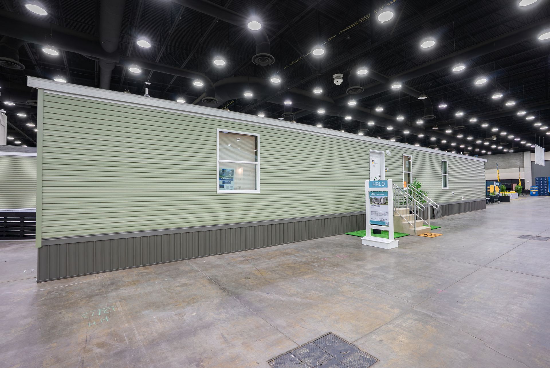 Large indoor exhibition hall with a green modular wall and small display stands under bright ceiling lights