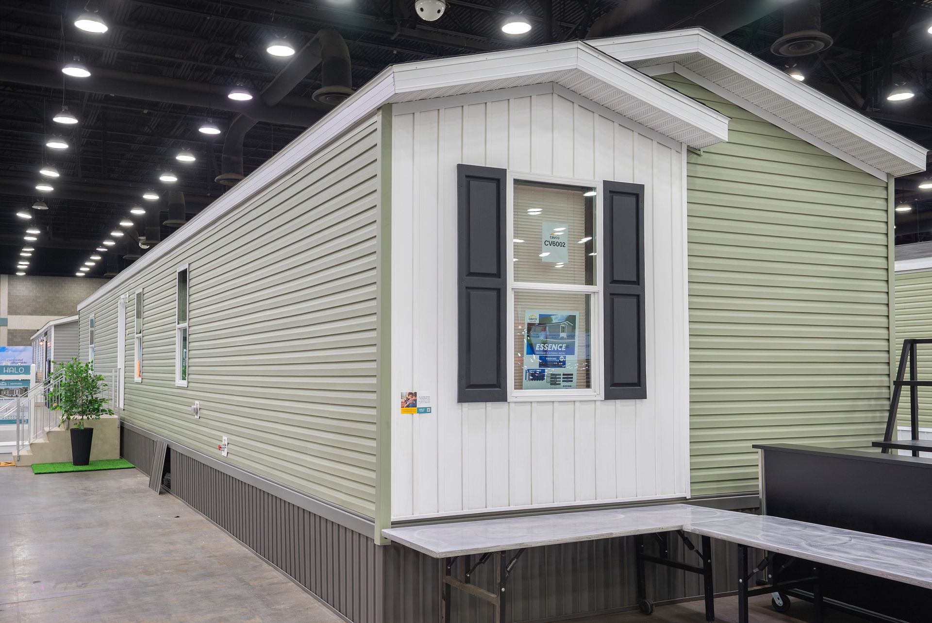 White manufactured home with gray siding and black shutters in an indoor display hall.