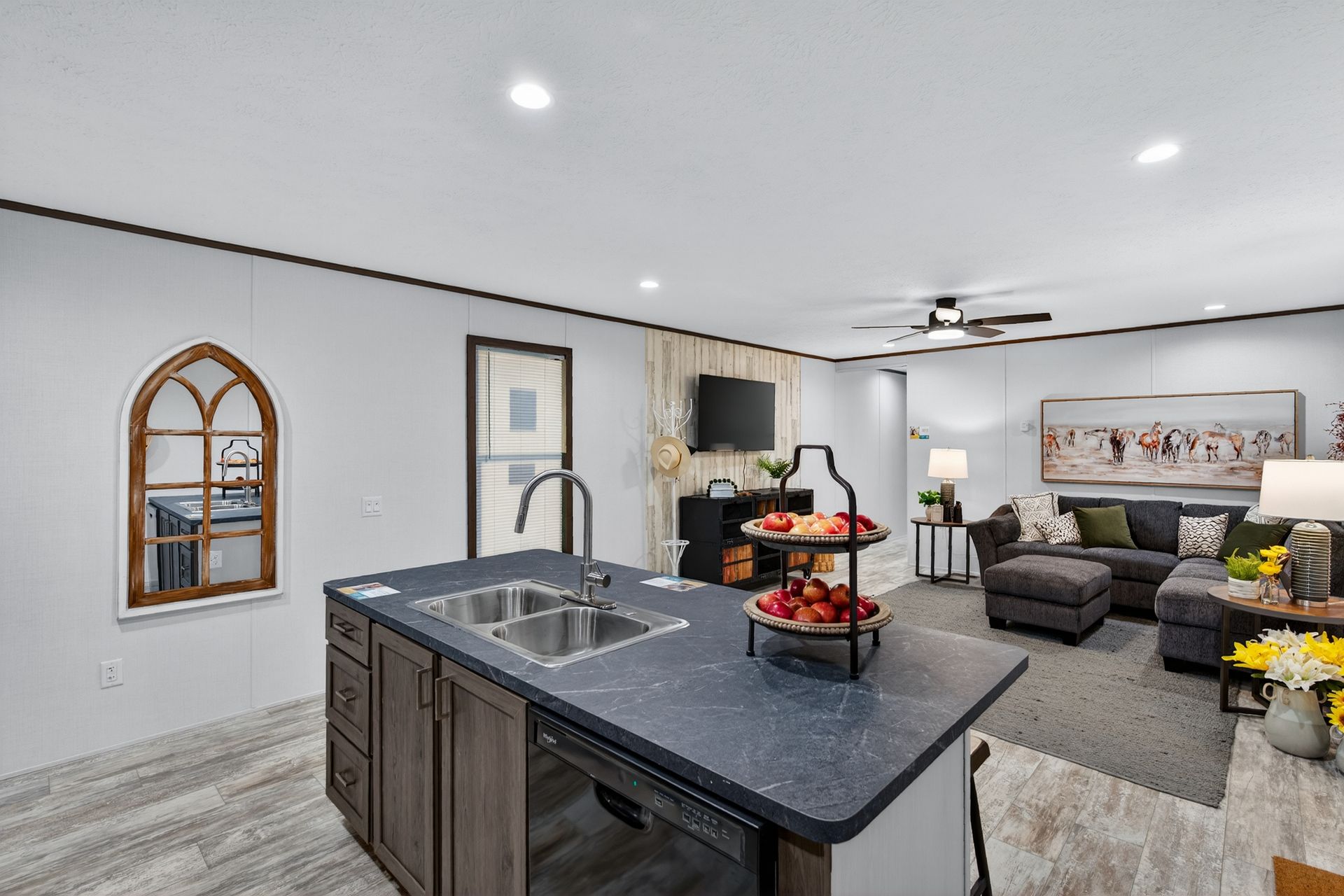 Open-concept modern kitchen and living room with dark island, gray sofa, and bright white walls.