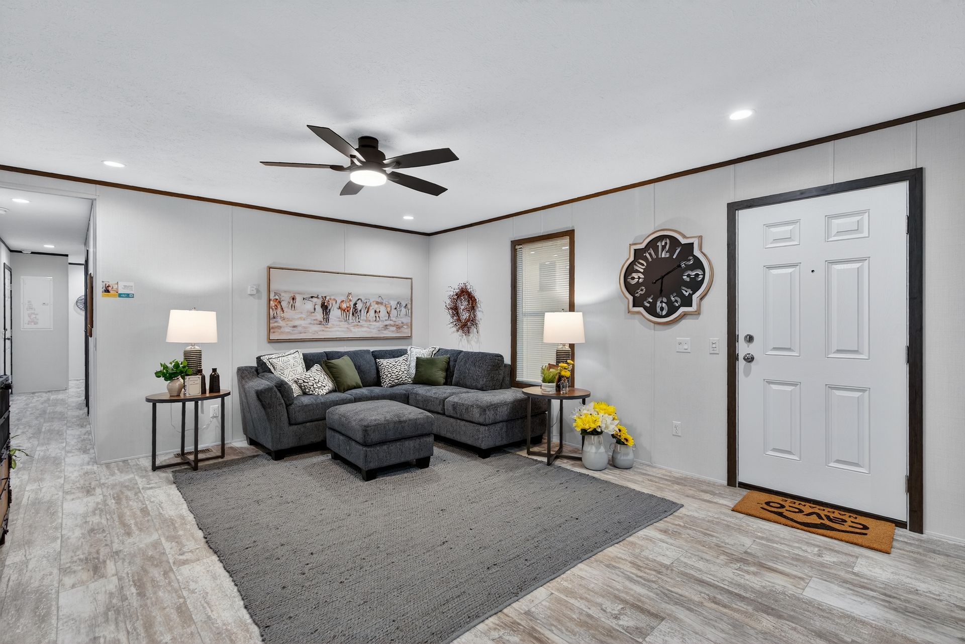 Bright living room with gray sectional sofa, ceiling fan, rug, wall art, and white front door