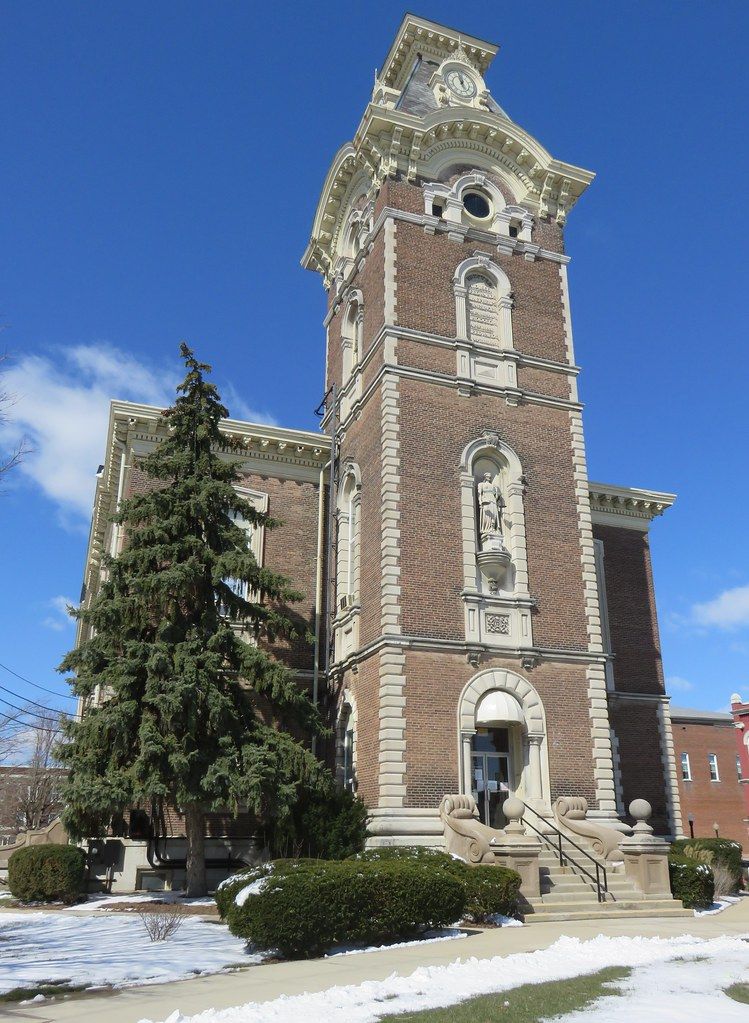 Brick church tower with a clock, arched entrance, and snow on the ground under a blue sky